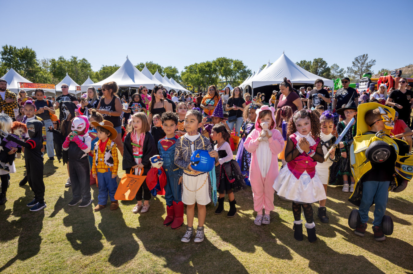 Children in Halloween costumes gather on the grass at the Southern Highlands Fall Festival, with white tent structures and crowds visible in the background.