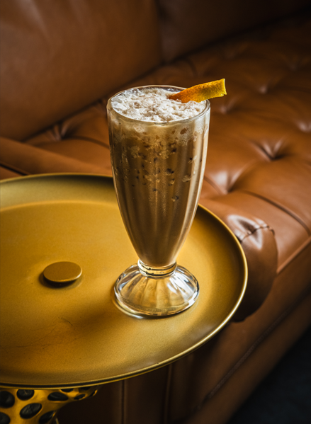 A fall-themed cocktail with ice and an orange peel garnish sits on a gold table at Las Vegas Distillery during their October events.