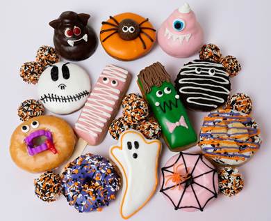 Pinkbox Doughnuts' Halloween-themed doughnut collection features festive designs including chocolate monsters, candy corn, ghost shapes, striped patterns, and sprinkled varieties decorated for the holiday season.